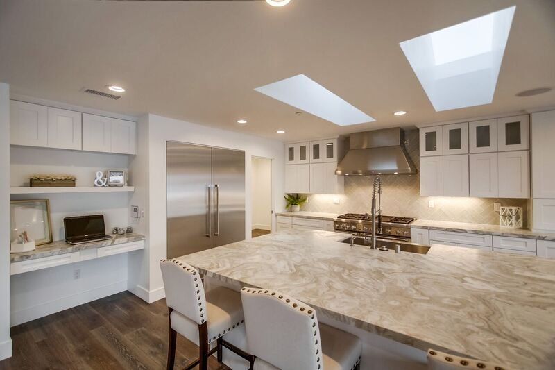 Modern kitchen with marble island, white cabinets, built-ins, skylights, and stainless steel range