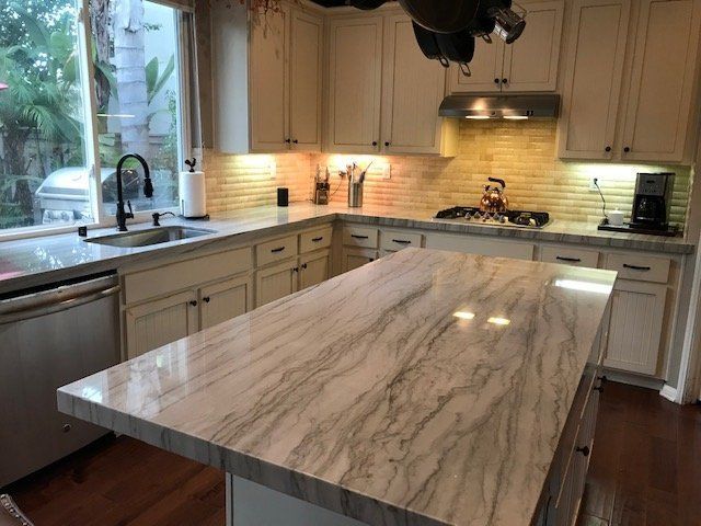 Modern kitchen with a large marble island, white cabinets, and a window over the sink
