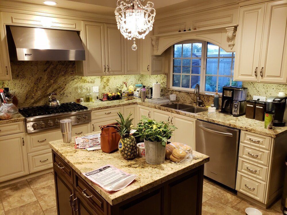 Bright cream kitchen with granite island, stainless appliances, chandelier, and window over the sink.