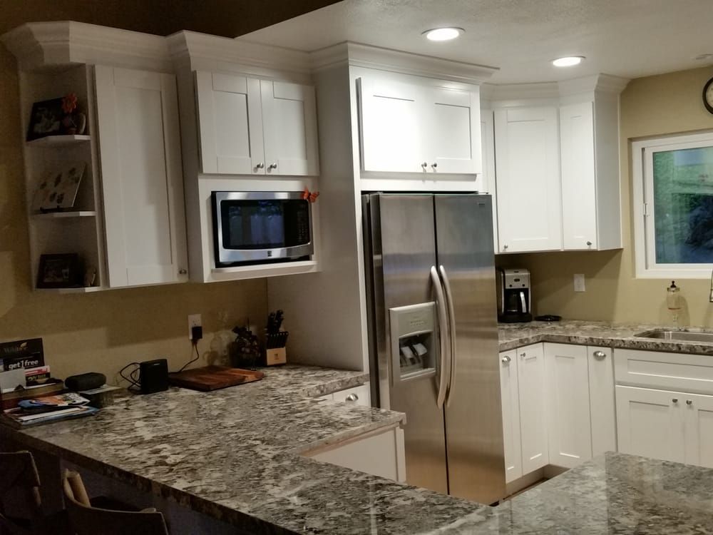 Modern kitchen with white cabinets, stainless steel refrigerator, granite countertops, and built-in microwave