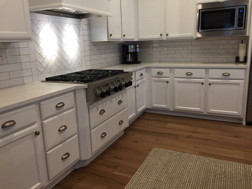 Bright white kitchen with gas range, tile backsplash, white cabinets, and hardwood floor