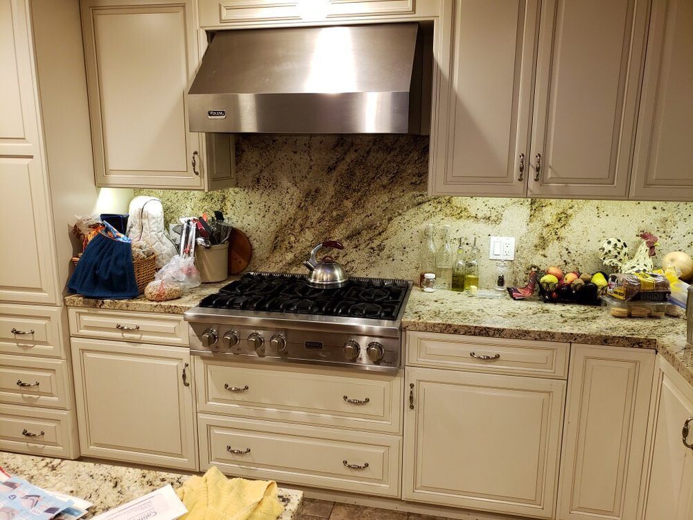 Modern kitchen with beige cabinets, granite counters, stainless range hood, and items on the left counter.