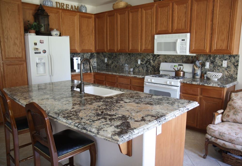 Modern kitchen with granite island, wooden cabinets, white appliances, and patterned backsplash