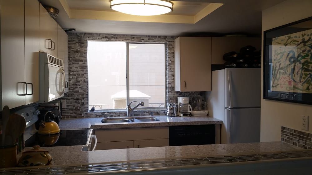 Kitchen with sink under a bright window, stone backsplash, and cabinets on either side.