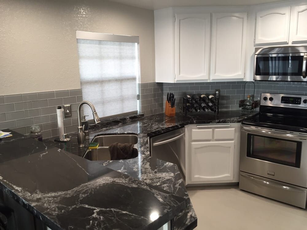 Modern kitchen with black marble counters, stainless steel appliances, white cabinets, and a tiled backsplash.