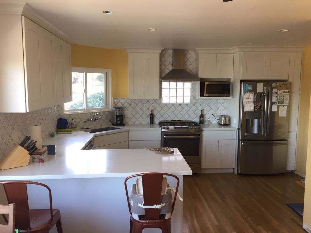 Bright modern kitchen with white cabinets, stainless fridge, island, and wooden floor.