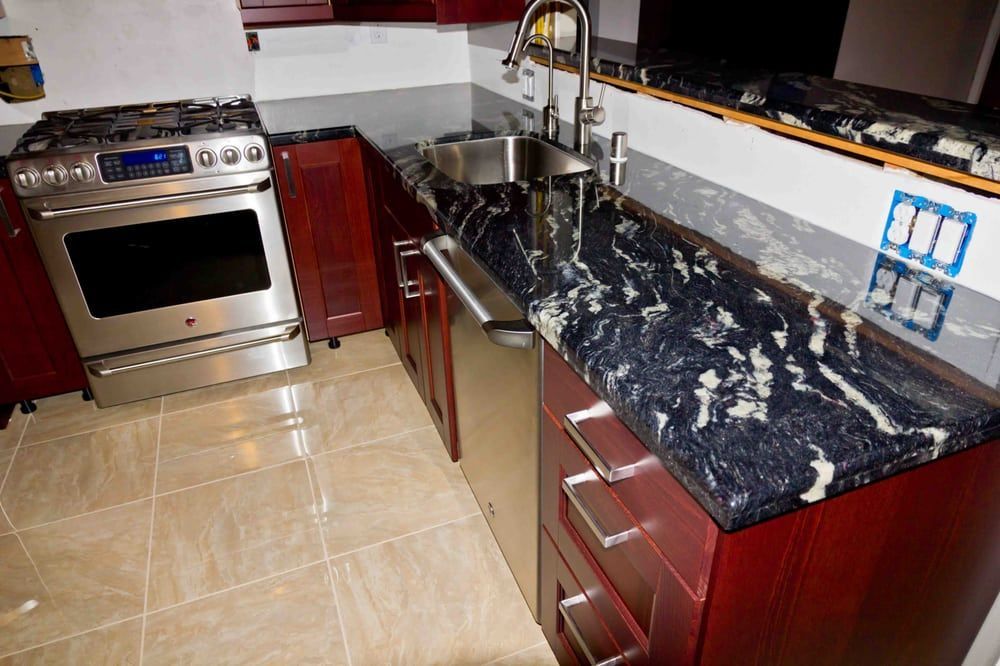 Modern kitchen with stainless steel stove, dark granite countertops, and red cabinets