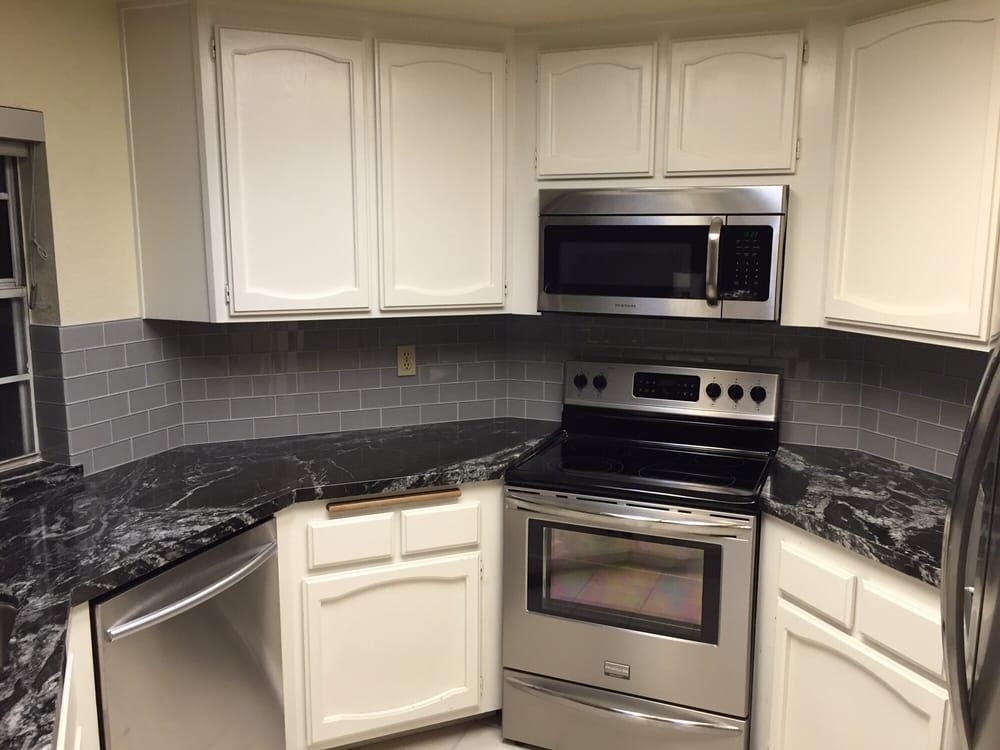 Modern kitchen with white cabinets, stainless steel oven and microwave, and dark granite countertops.