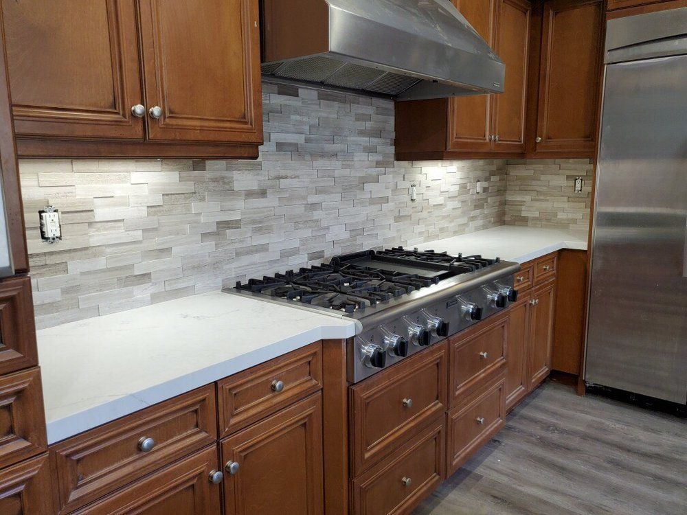 Modern kitchen with wood cabinets, white countertops, a gas range, stainless hood, and gray tile backsplash