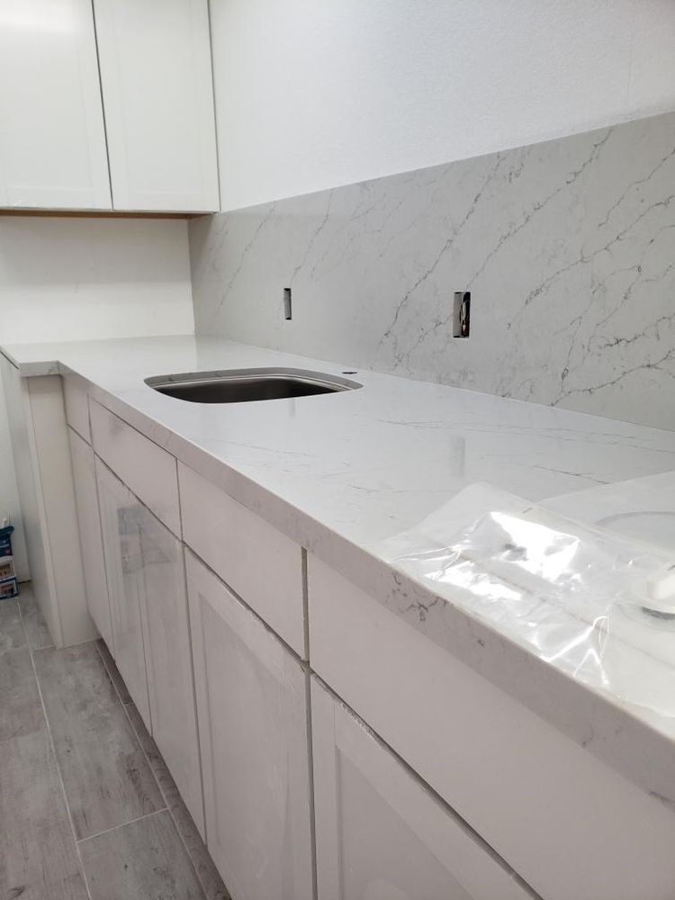 Modern white kitchen with marble-look countertop, built-in sink, and light wood lower cabinets.