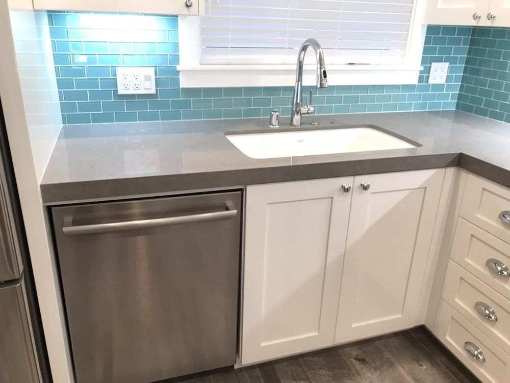 Modern kitchen sink area with white cabinets, gray countertop, and blue tile backsplash