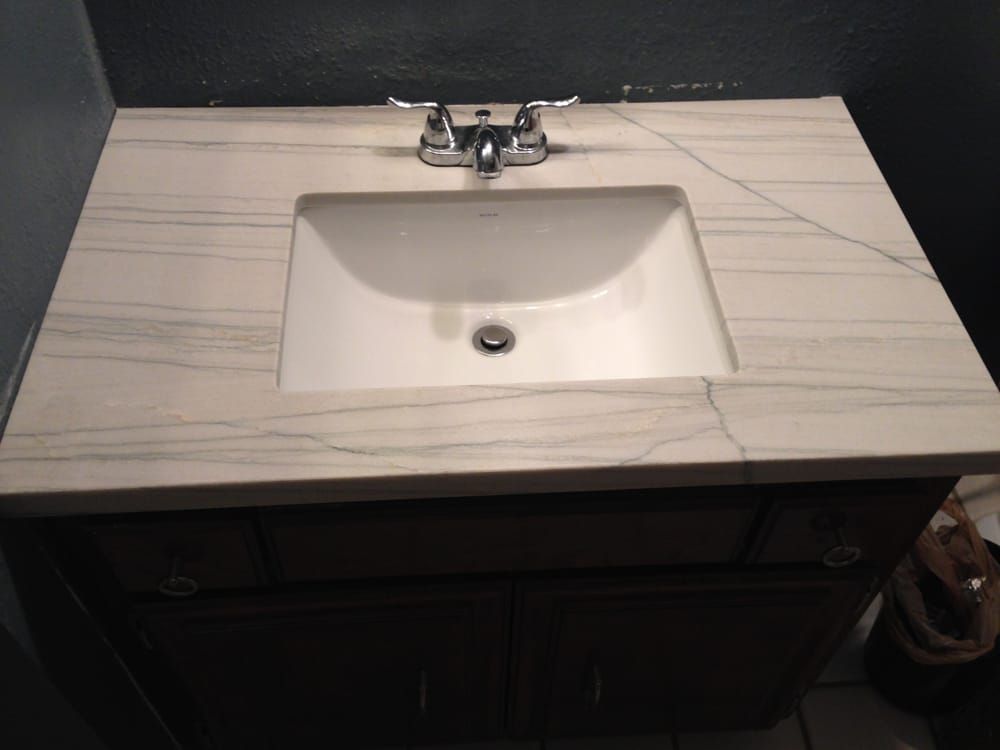 Bathroom sink with white countertop, chrome faucet, and dark vanity cabinet below.