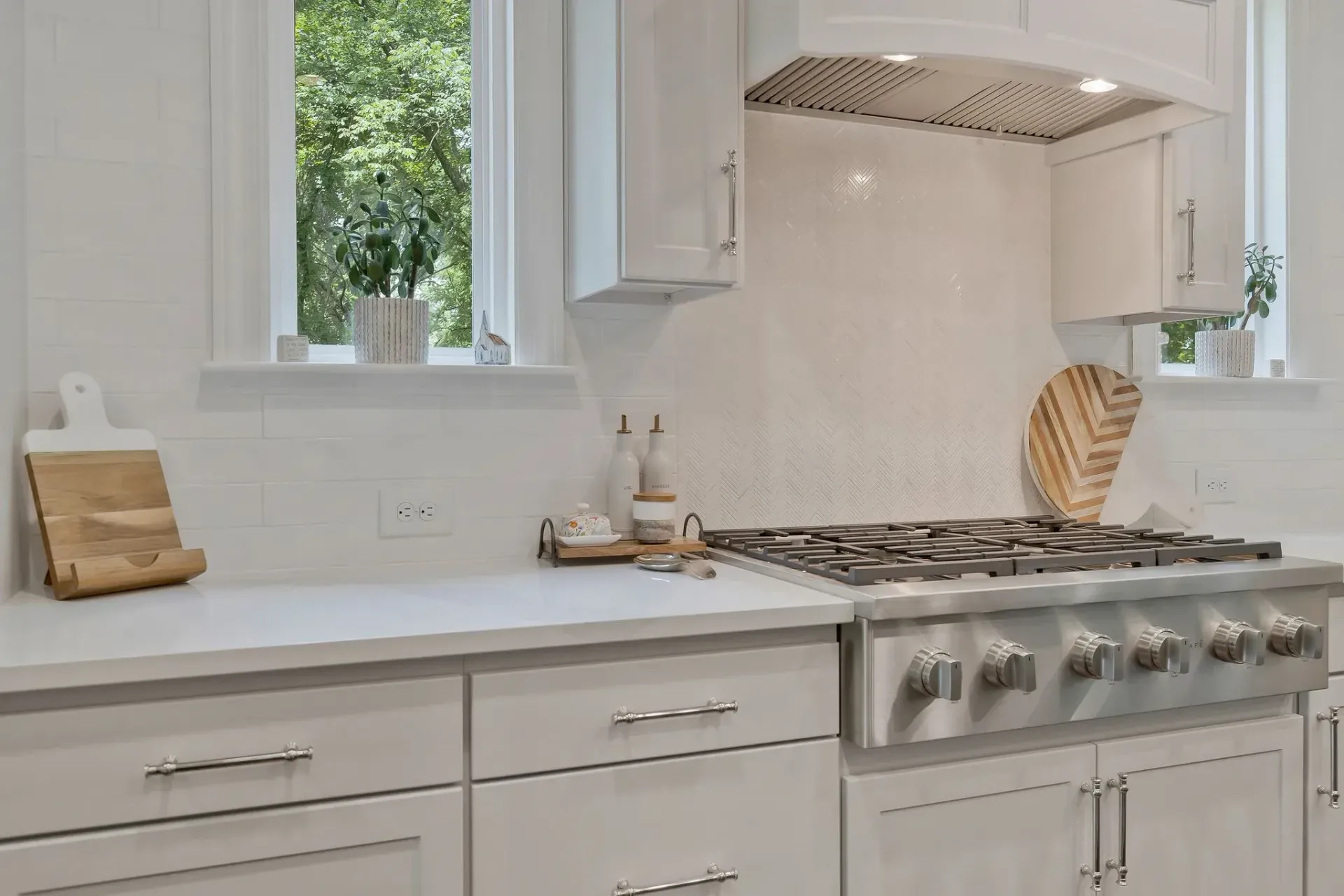 Bright white kitchen with marble counters, stainless range, and open windows letting in daylight
