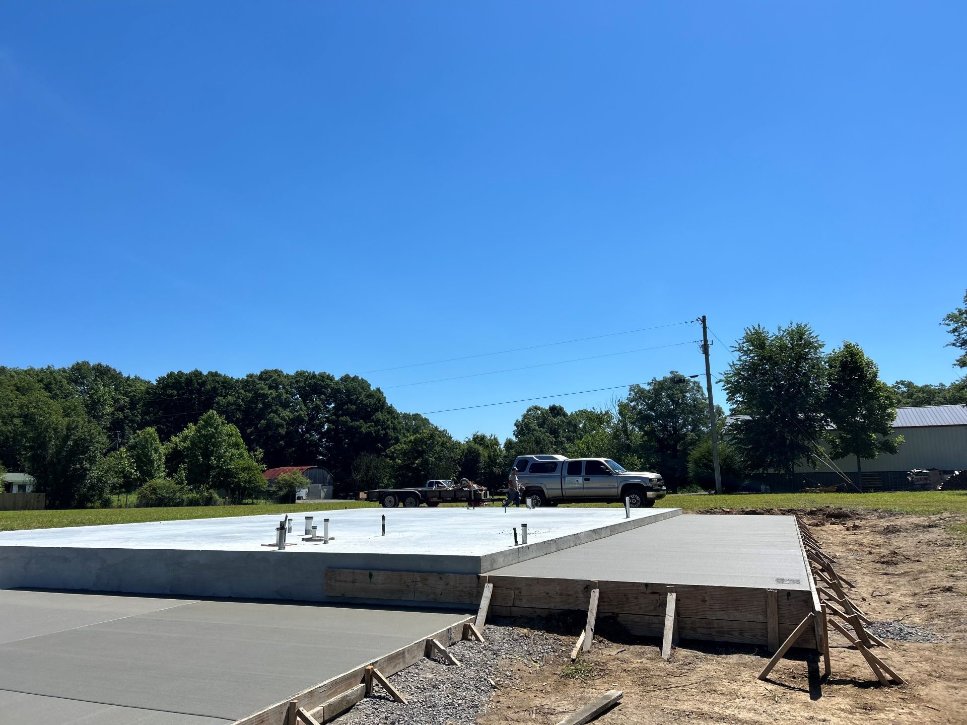Partially built concrete slab under a clear blue sky, with workers and a boom truck in the background