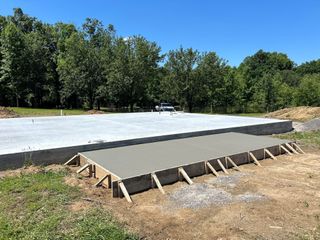 Fresh concrete slab with a small ramp form, set in a wooded outdoor construction area.
