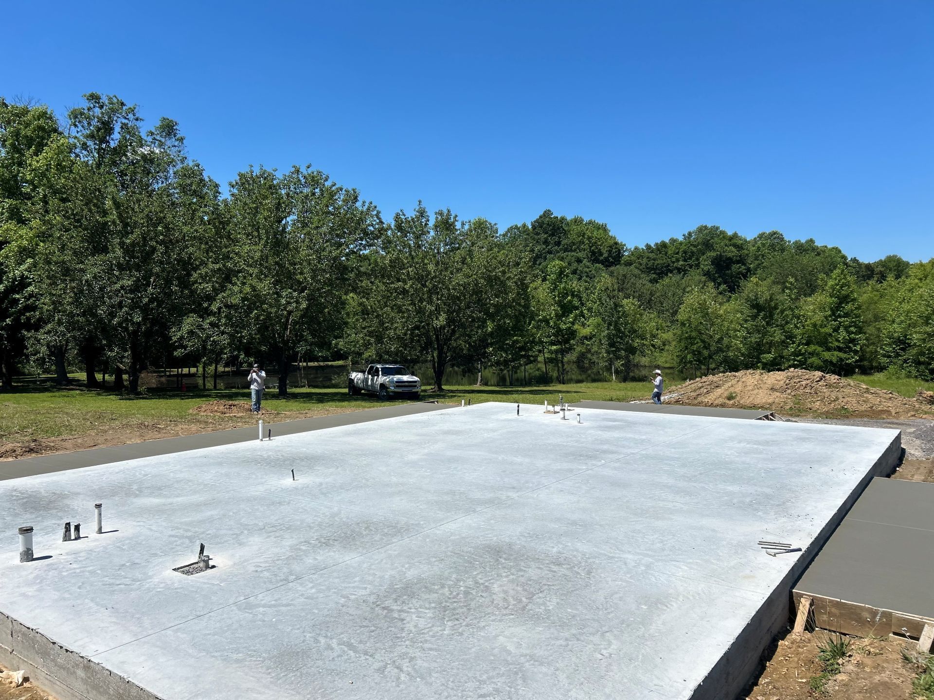 Concrete foundation slab on a wooded lot under a clear blue sky
