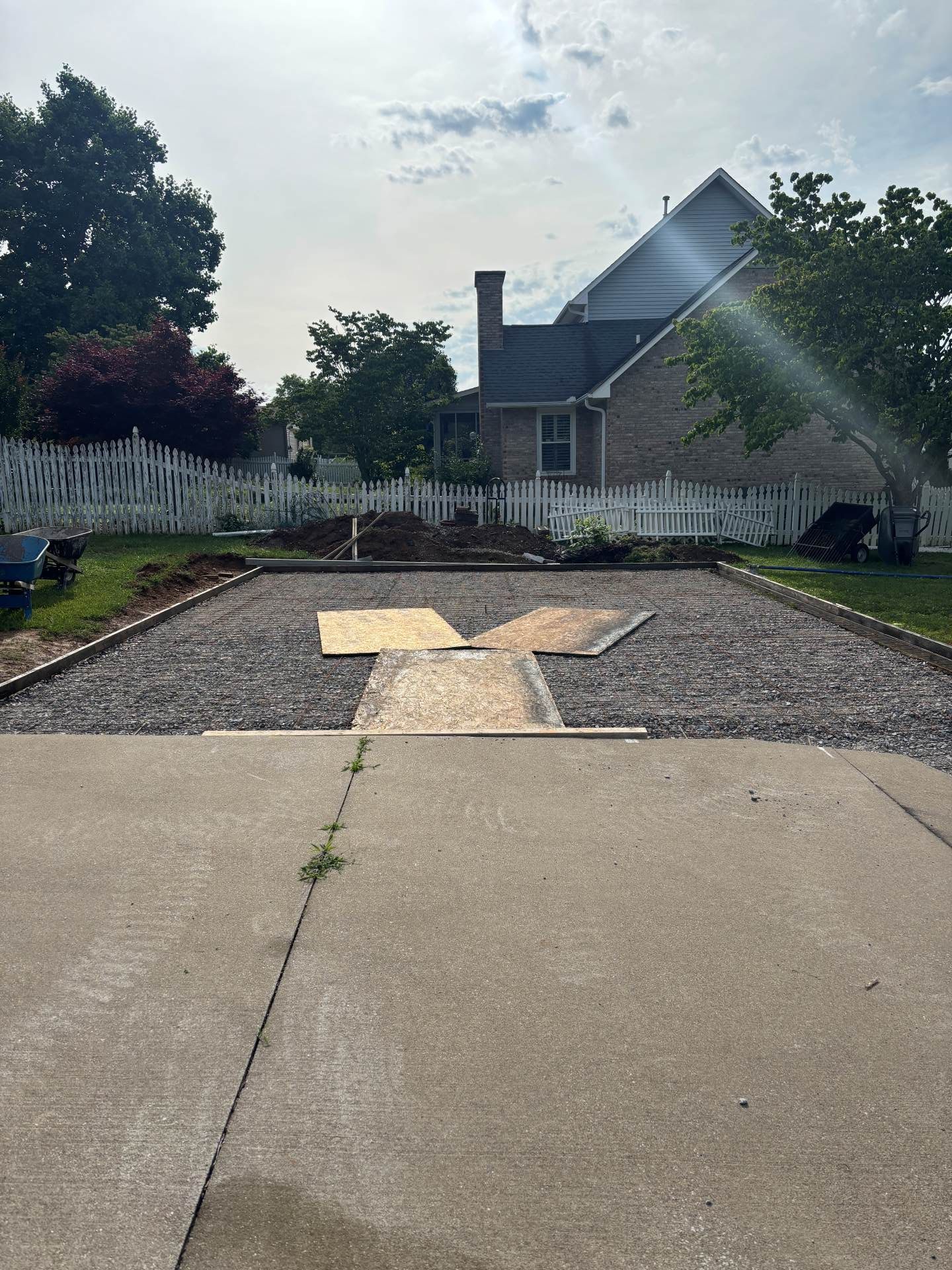 Driveway leading to a gravel courtyard with a white fence and house in the background.