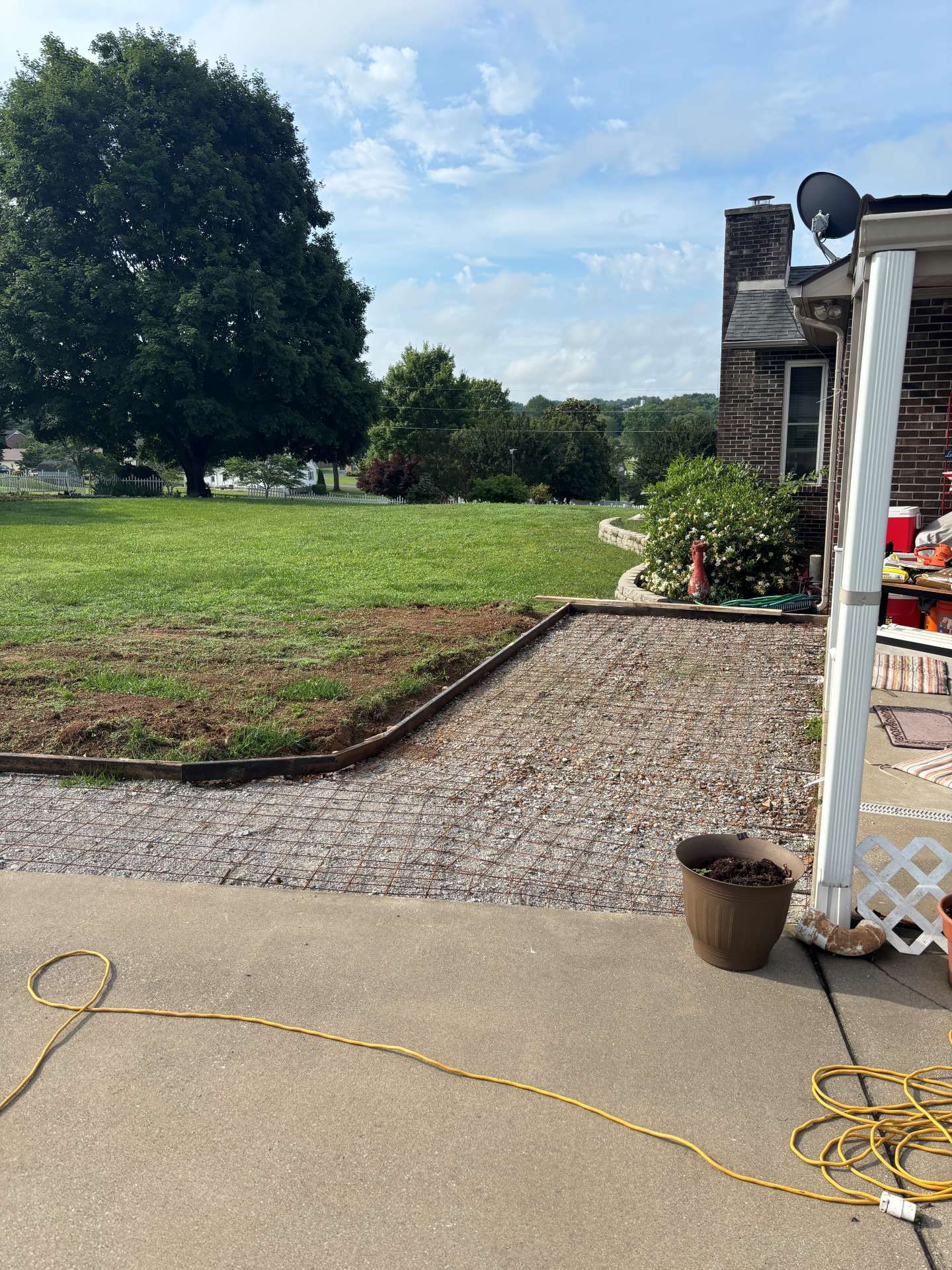 Patio leading to a grassy yard with a large tree, gravel path, and house exterior on the right