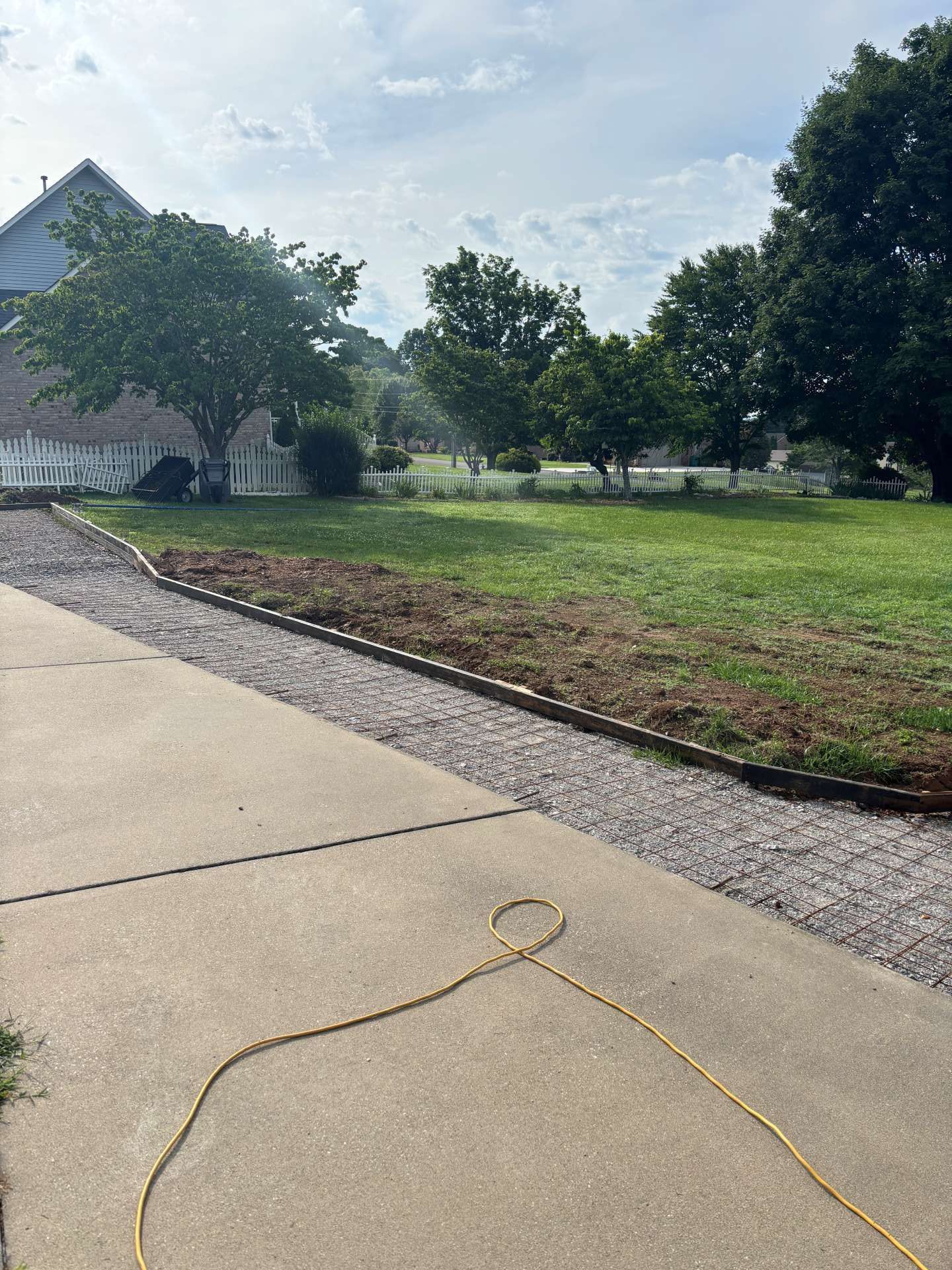 Suburban sidewalk beside a grassy lawn and trees, with a yellow cord on the pavement.