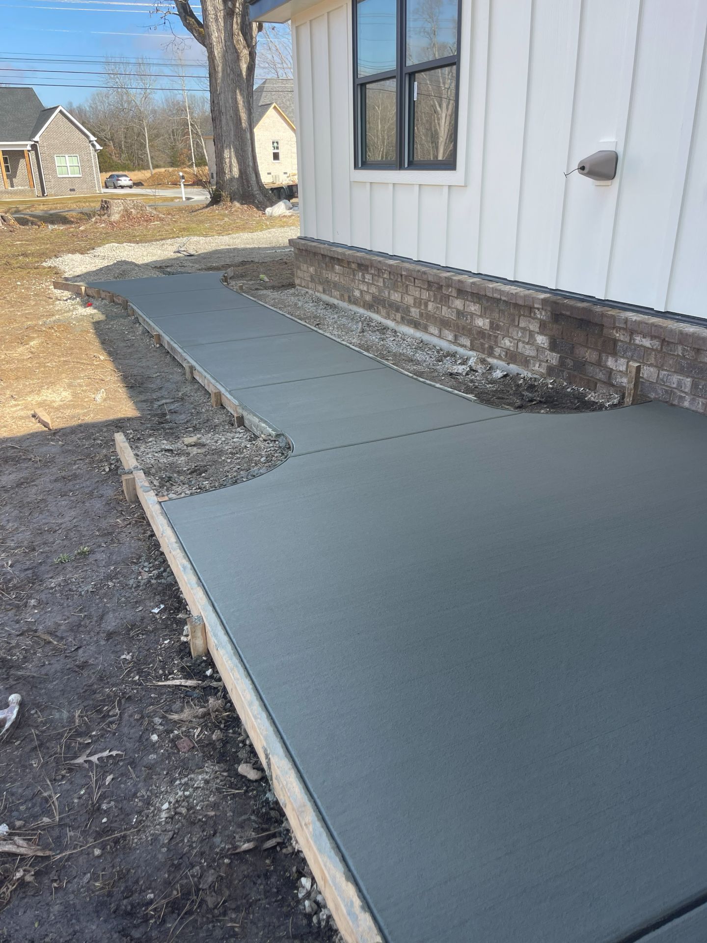 Fresh gray concrete walkway beside a white house with gravel edging and dirt yard