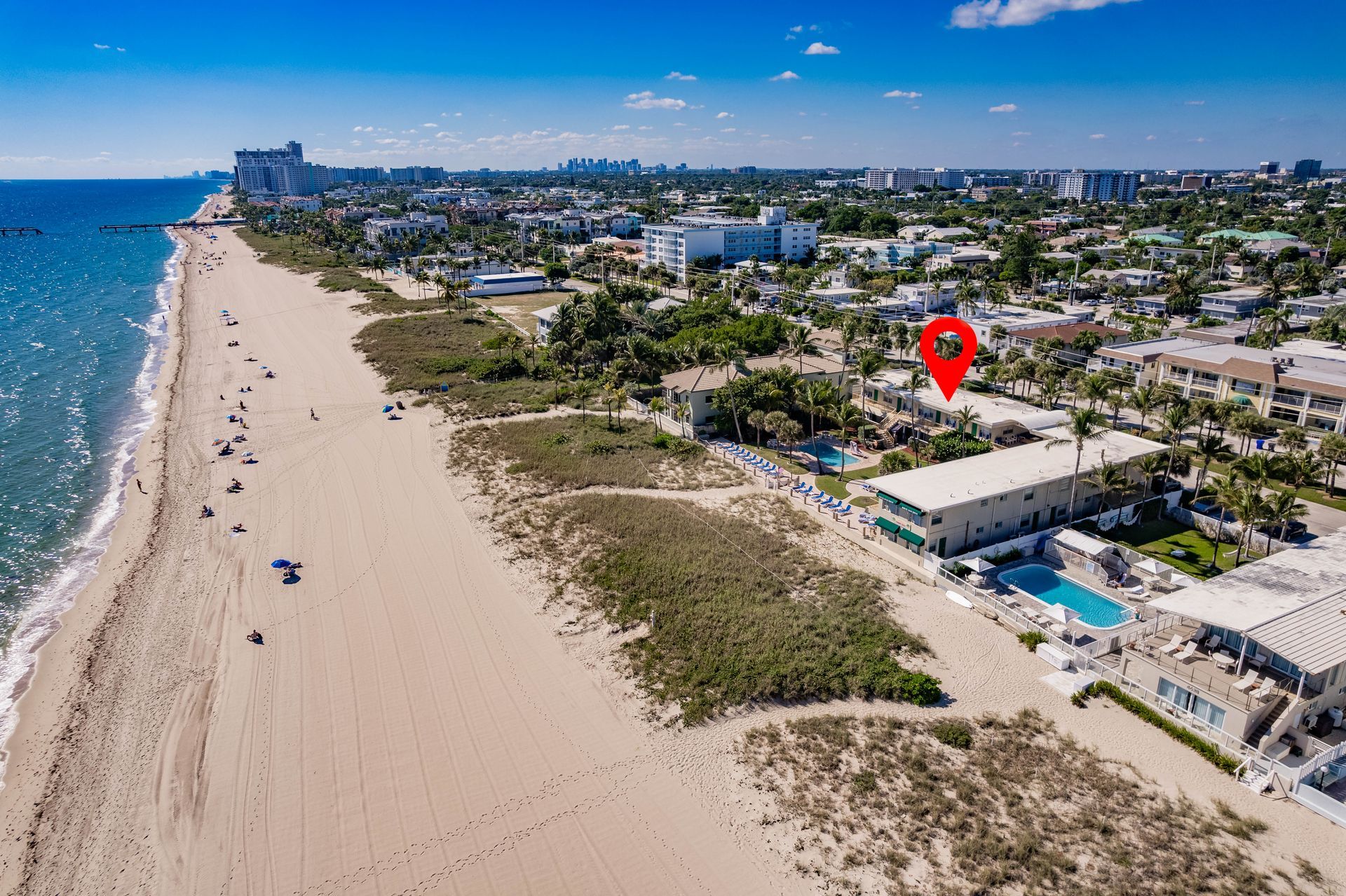 Aerial view of a beach with buildings, a pool, and a red location marker.