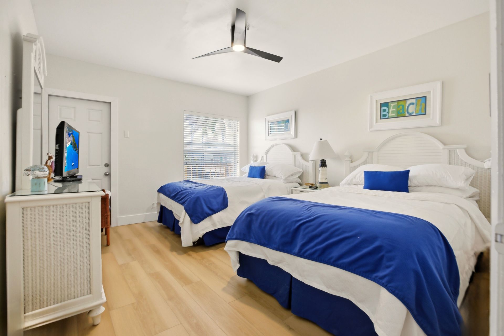 Yellow-walled hotel room with bed, table, chairs, and TV. Window, ceiling fan, and tiled floor.
