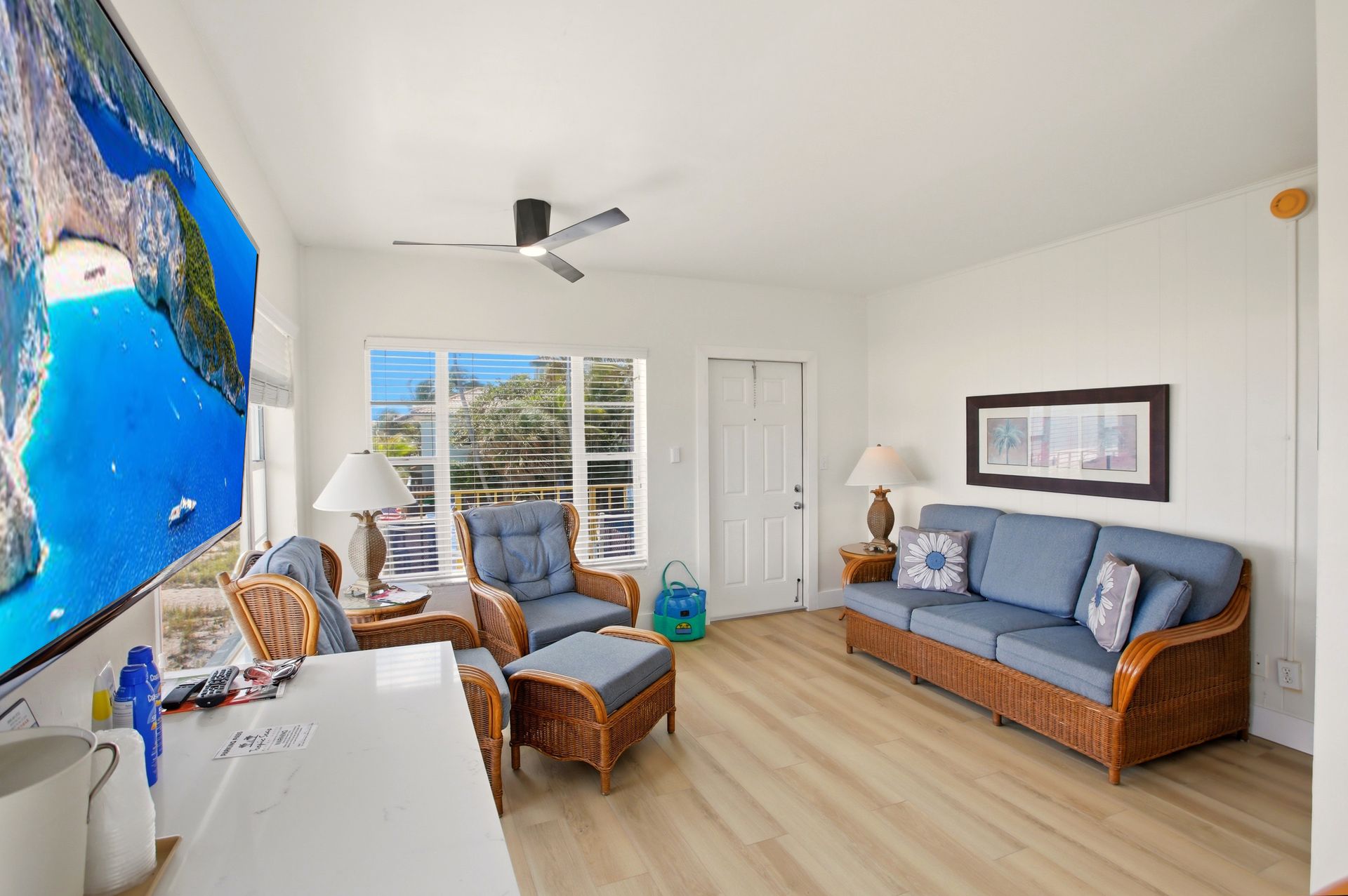 Bright living room with blue sofa, wicker chair, ocean mural, and large window overlooking water