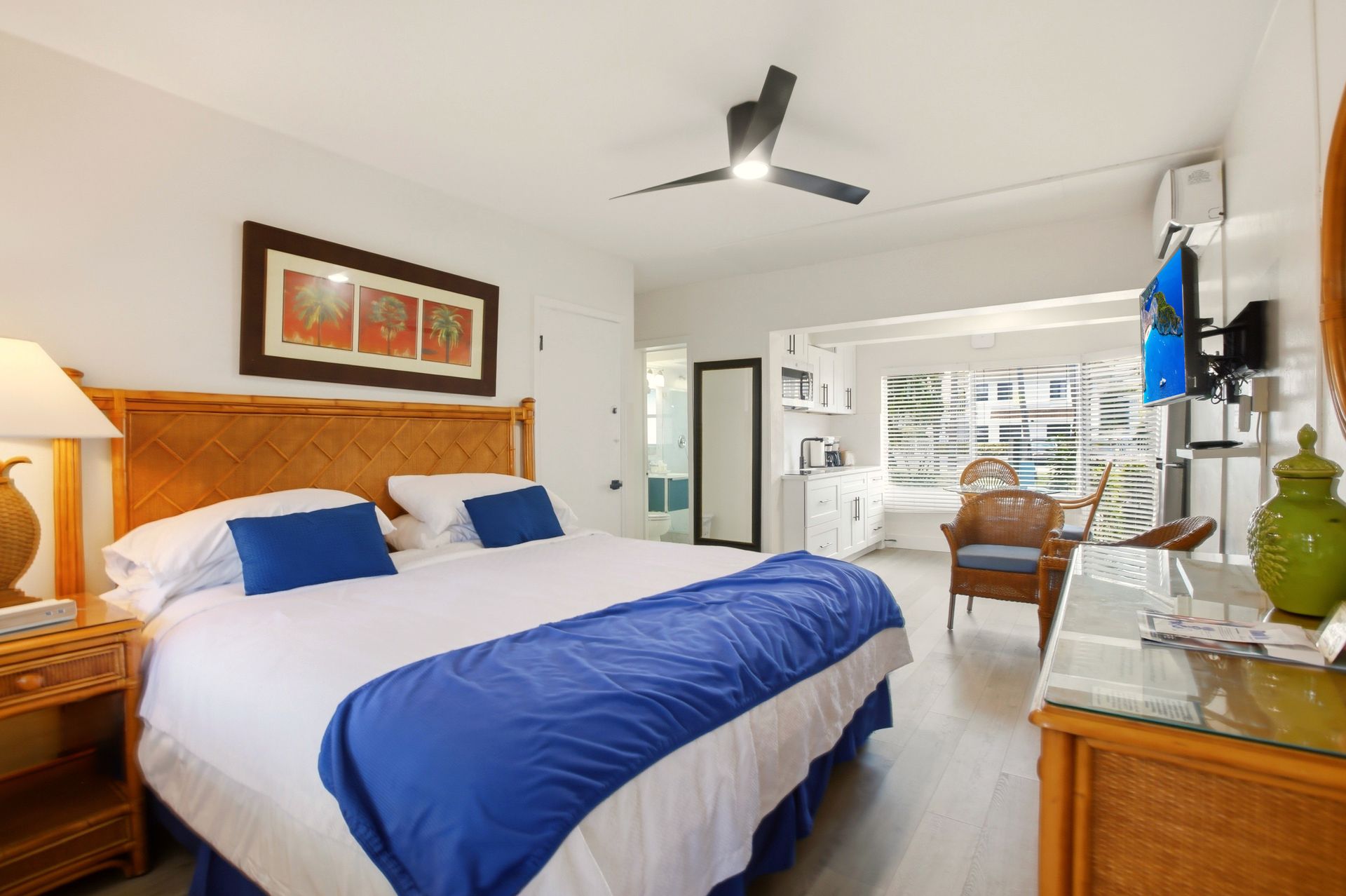 Bright bedroom with blue bedding, wooden furniture, ceiling fan, and a balcony view through open doors
