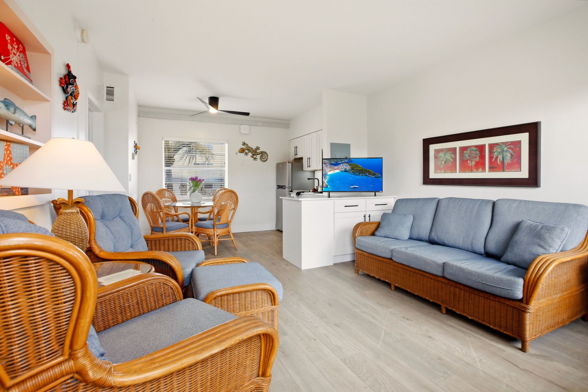Bright living room with wicker chairs, blue sofa, TV, and open kitchen in the background
