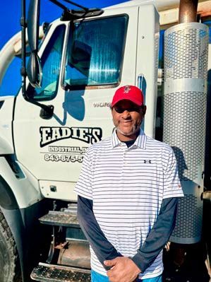 Man in red hat and striped shirt stands by a truck with