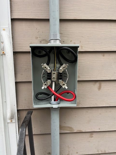 A electrical box is attached to a metal pole on the side of a house installed by Patriot Electrical Solutions.