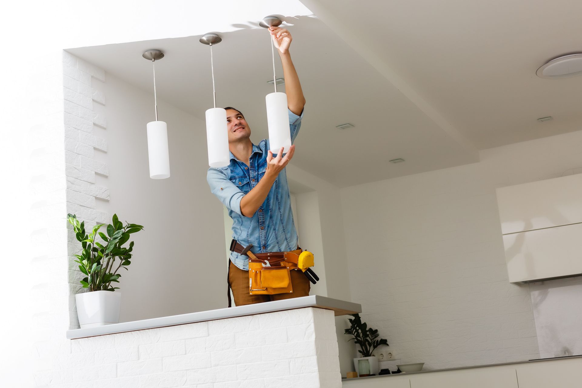 An electrician installing pendant light fixtures on a ceiling. An electrician installing pendant light fixtures on a ceiling.