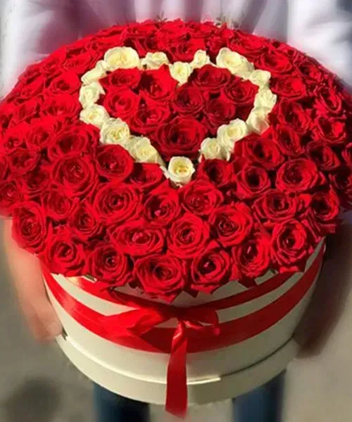 Caja redonda de rosas rojas con un arreglo de rosas blancas en forma de corazón en la parte superior.