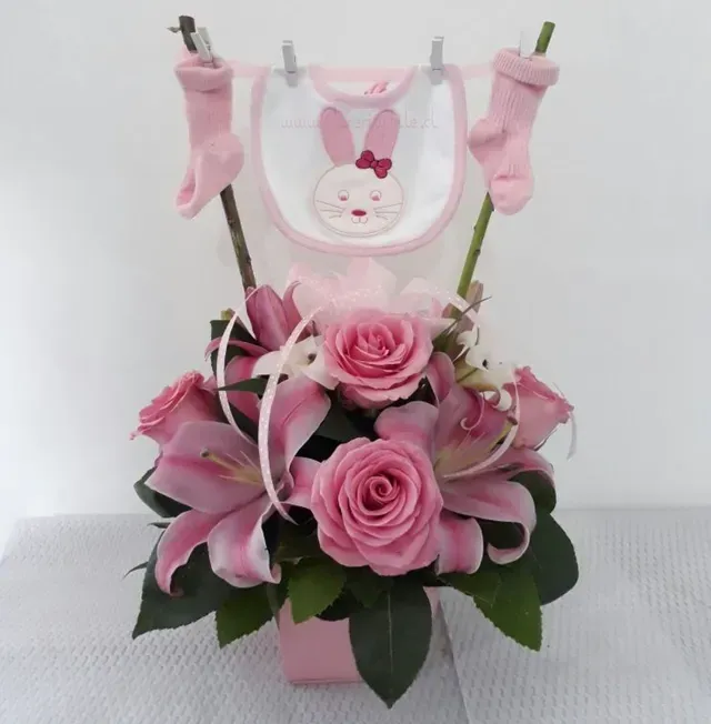 Arreglo floral de rosas rosadas con un babero de conejito y calcetines rosas en ramas, en un jarrón rosa.
