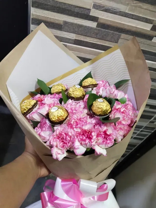 Ramo de mano de flores rosas con bombones envueltos en papel dorado y un lazo rosa.