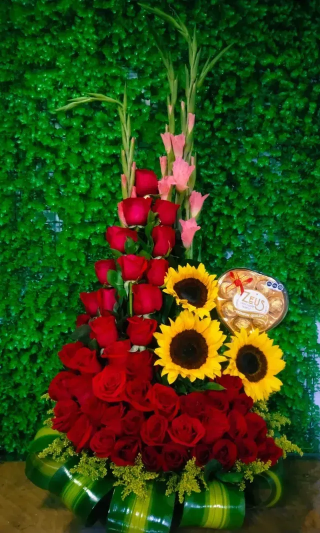 Rosas rojas y girasoles dispuestos en un ramo decorativo con flores rosas y hojas verdes.