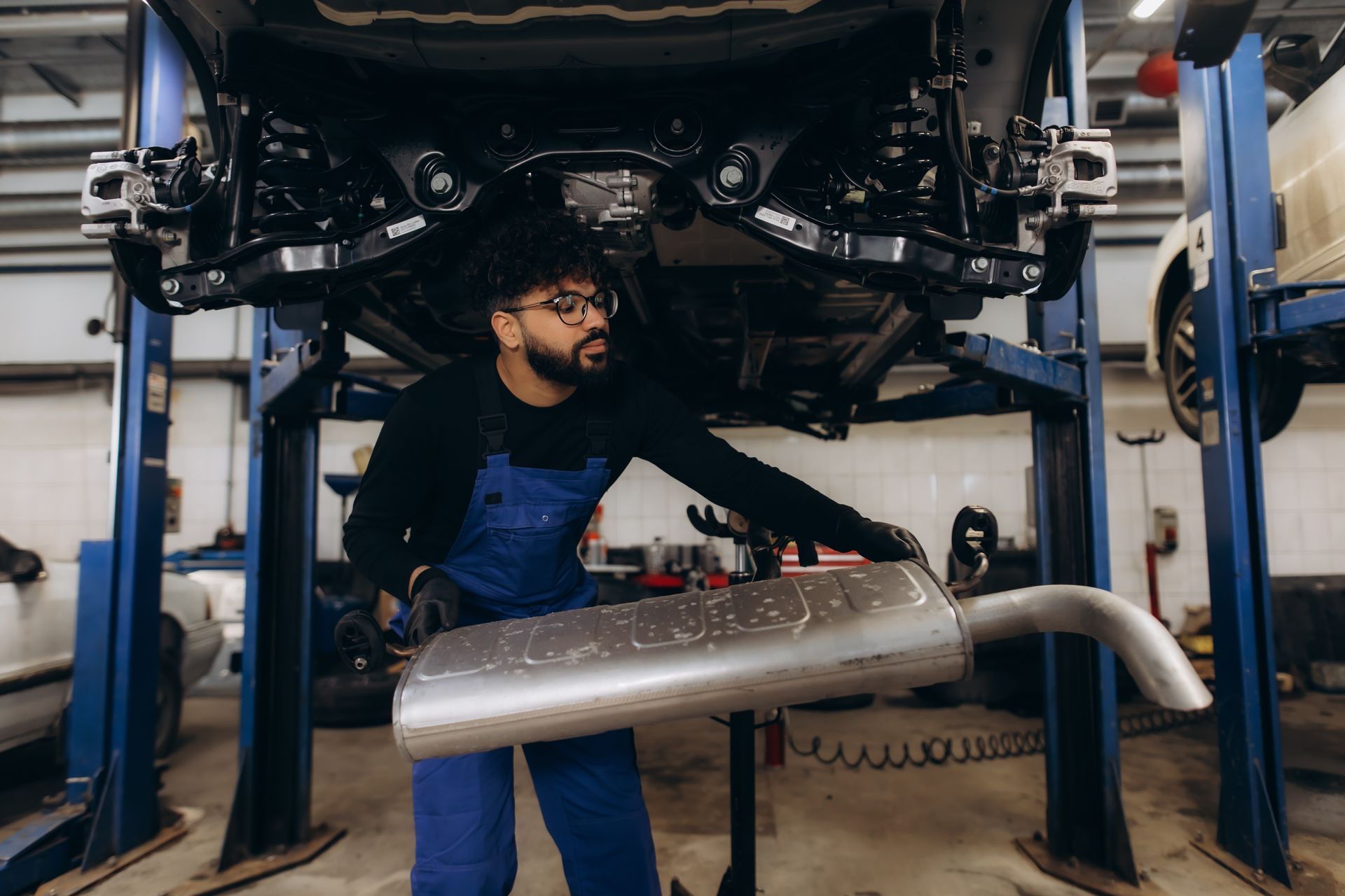 An auto mechanic is replacing a car exhaust muffler in a garage.