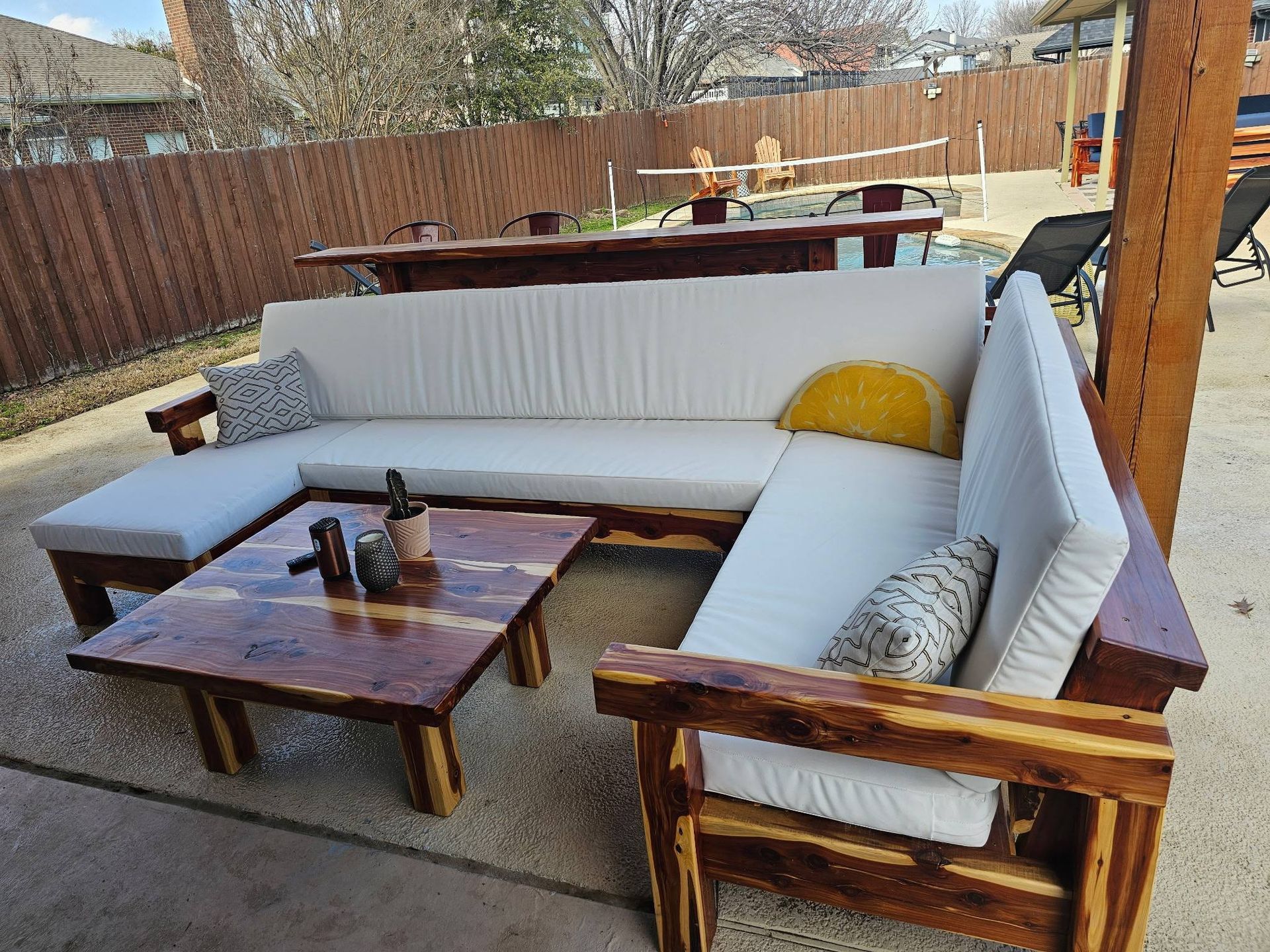 L-shaped wooden outdoor sectional with white cushions and a matching square coffee table on a concrete patio.