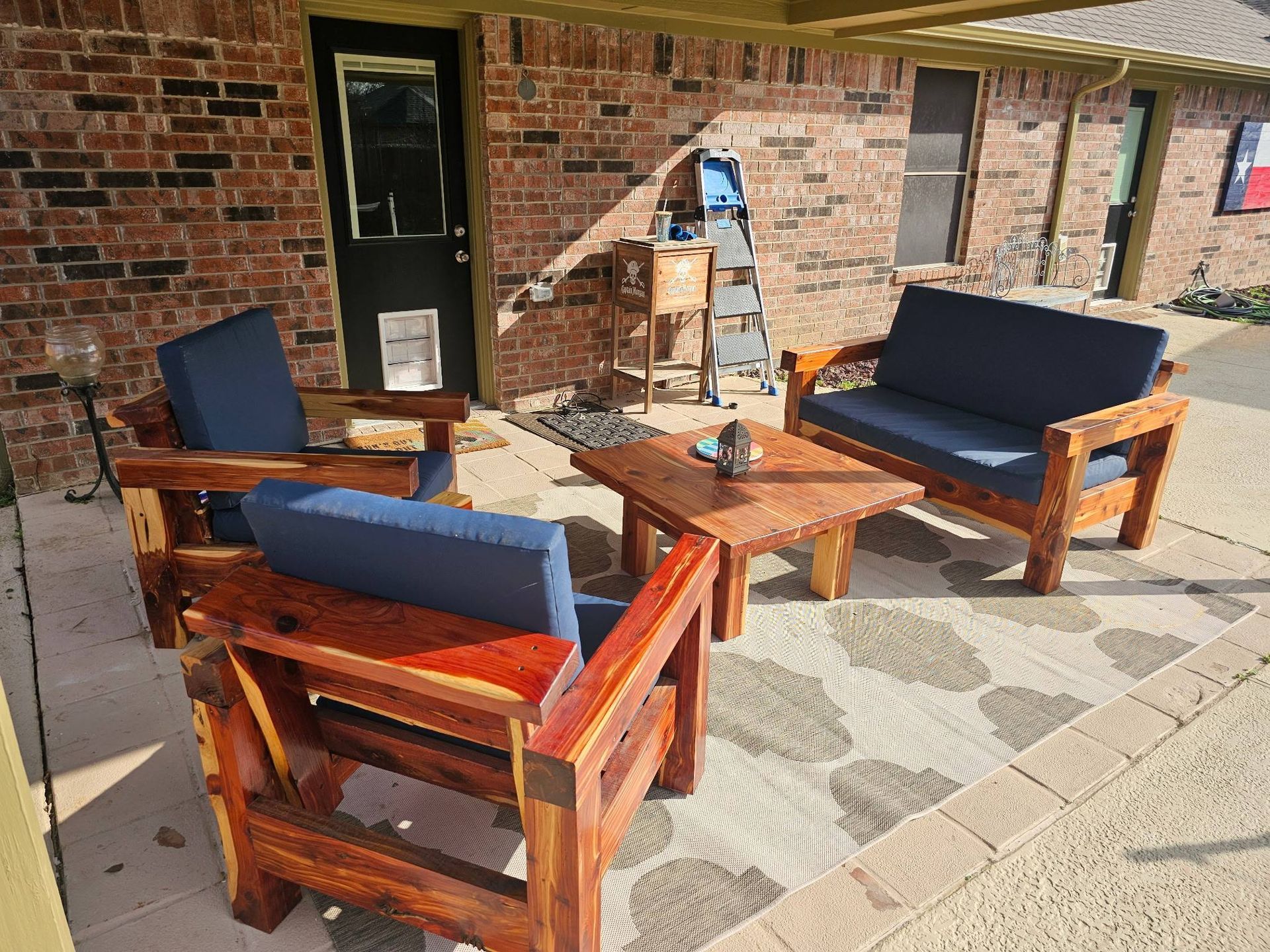 Outdoor patio furniture with dark blue cushions on a rug in front of a brick house.