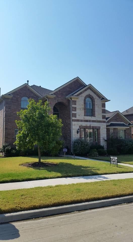 A two-story house with a brick exterior and stone accents, featuring a green lawn and a small tree in the front yard.