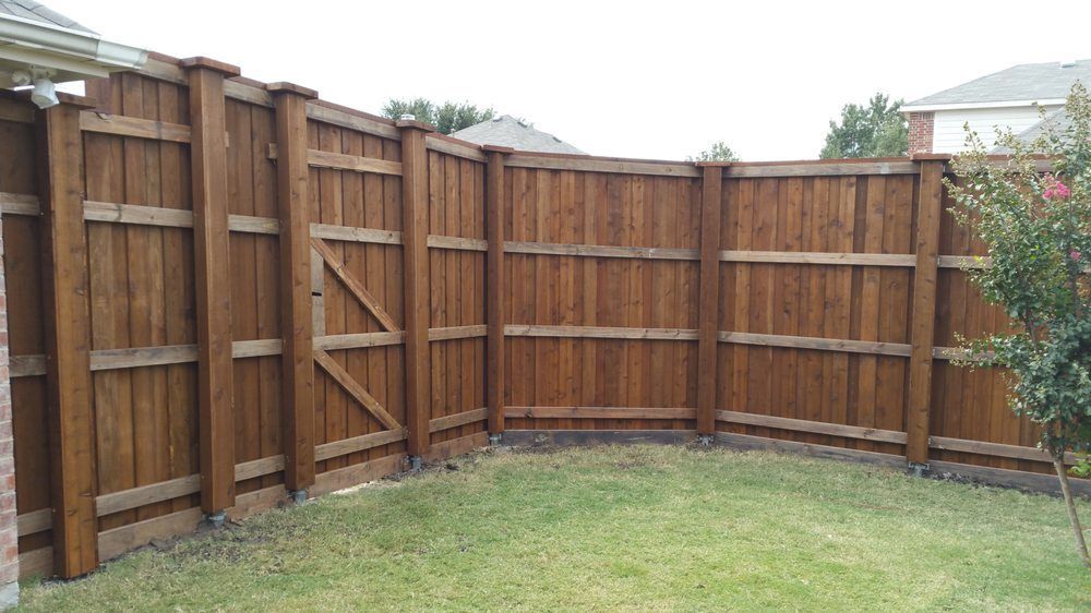 A stained wooden privacy fence with vertical boards and horizontal support beams, forming an L-shape in a backyard.