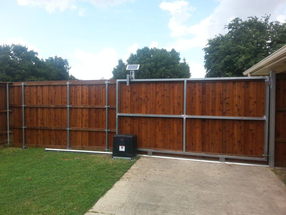 A wooden sliding gate with a metal frame, motor, and small solar panel, installed next to a matching wood fence.