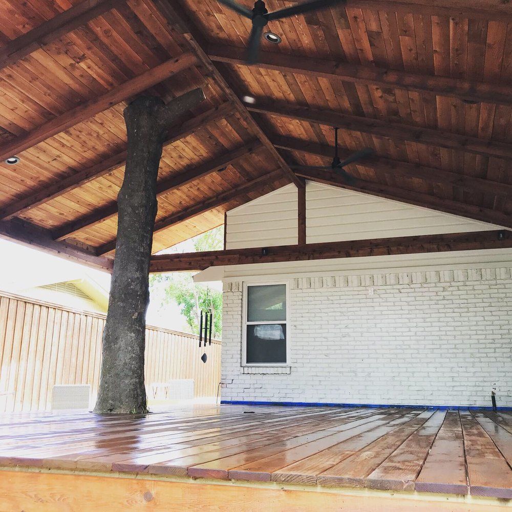 A wooden deck with a tree growing through the roof of its covered porch, attached to a white brick house.