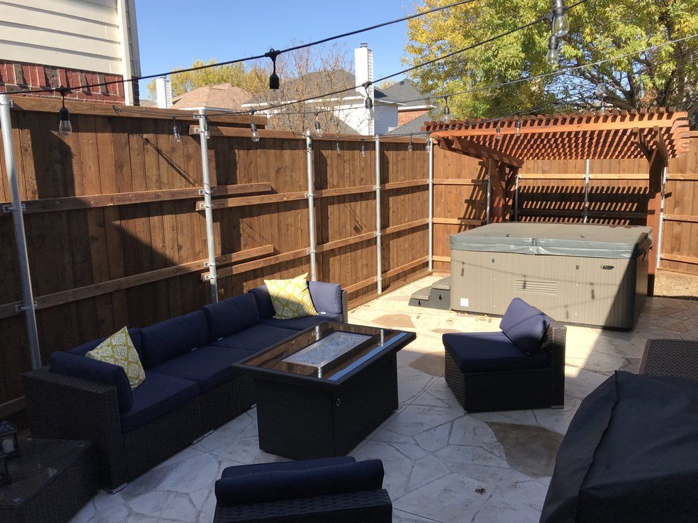 A backyard patio featuring an outdoor sectional sofa, fire pit, single chair, and a hot tub under a wooden pergola.