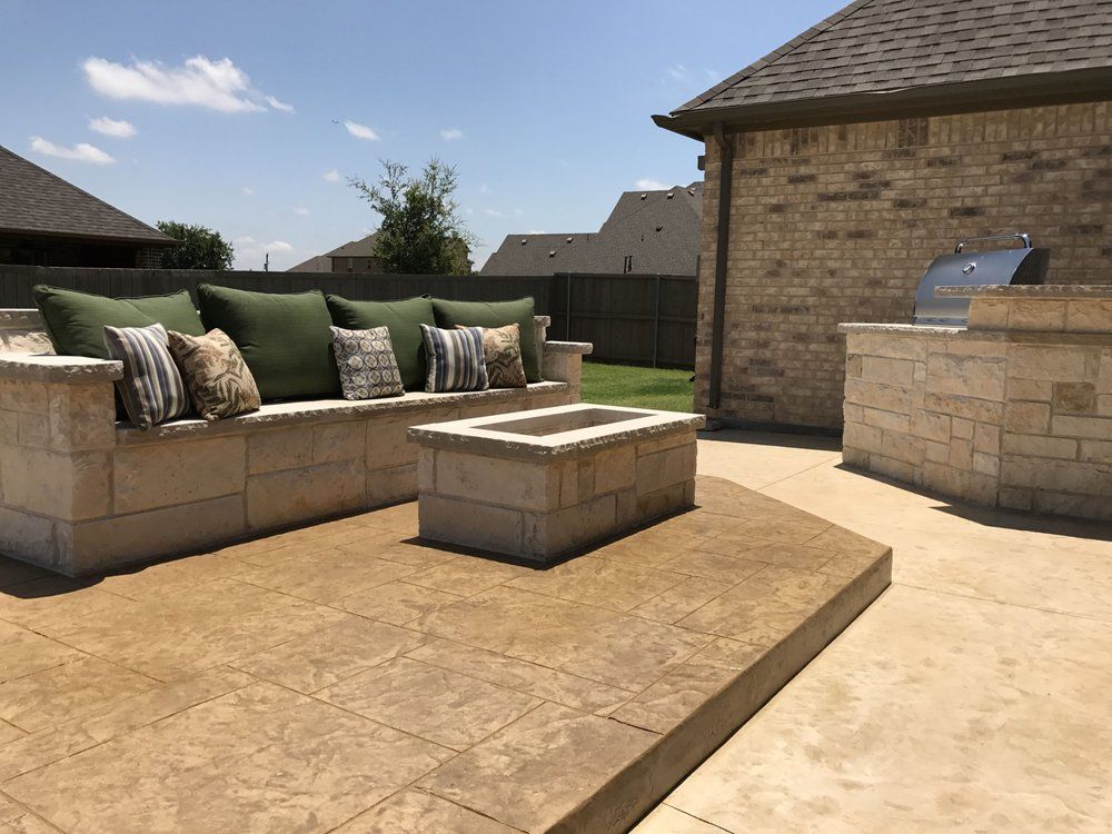 Outdoor patio with a stone-built sofa, matching fire pit, and stone grill station on a stamped concrete deck.
