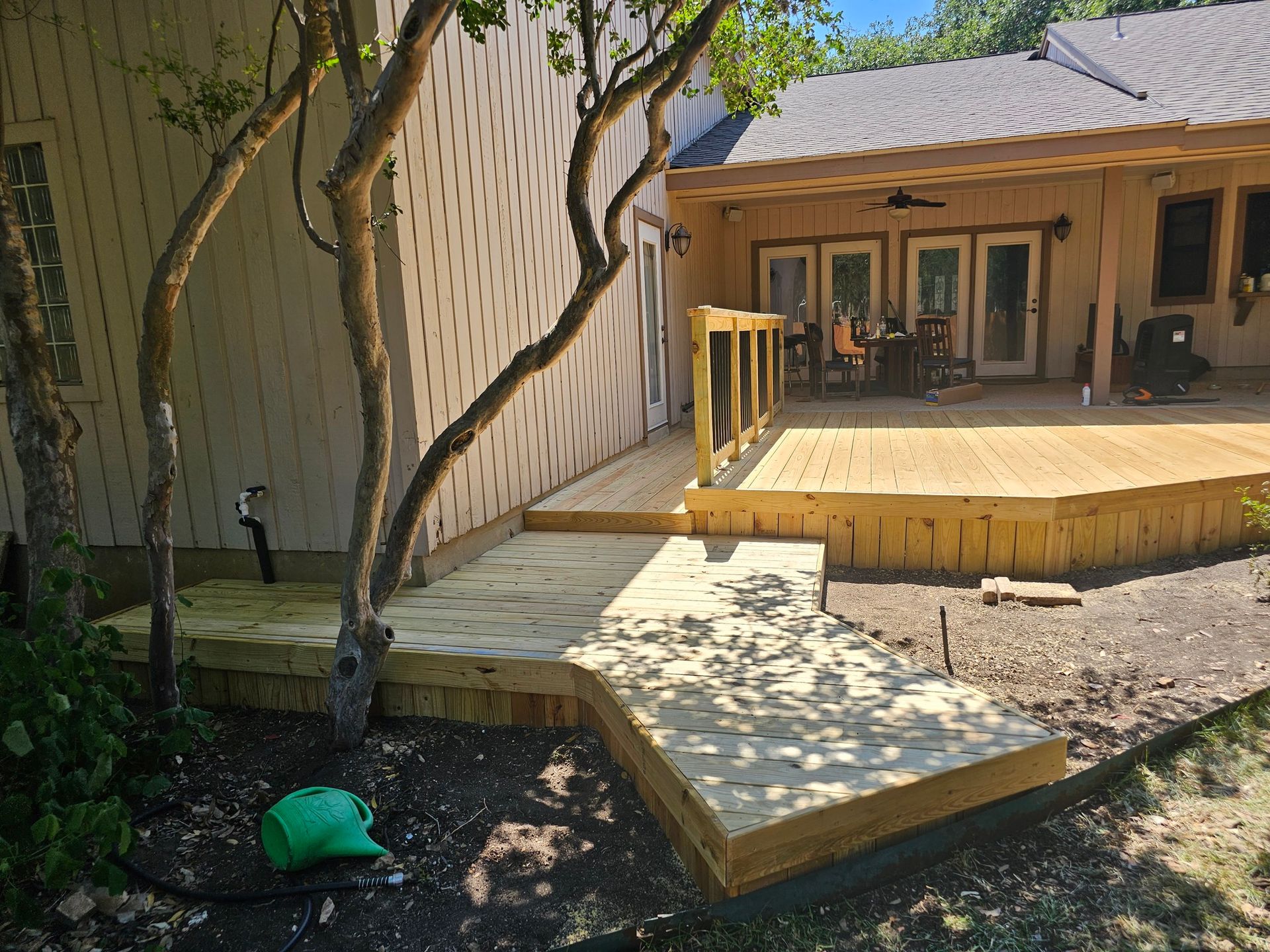 Newly built wooden deck with access ramp and stairs, attached to a light-colored house with a covered patio.