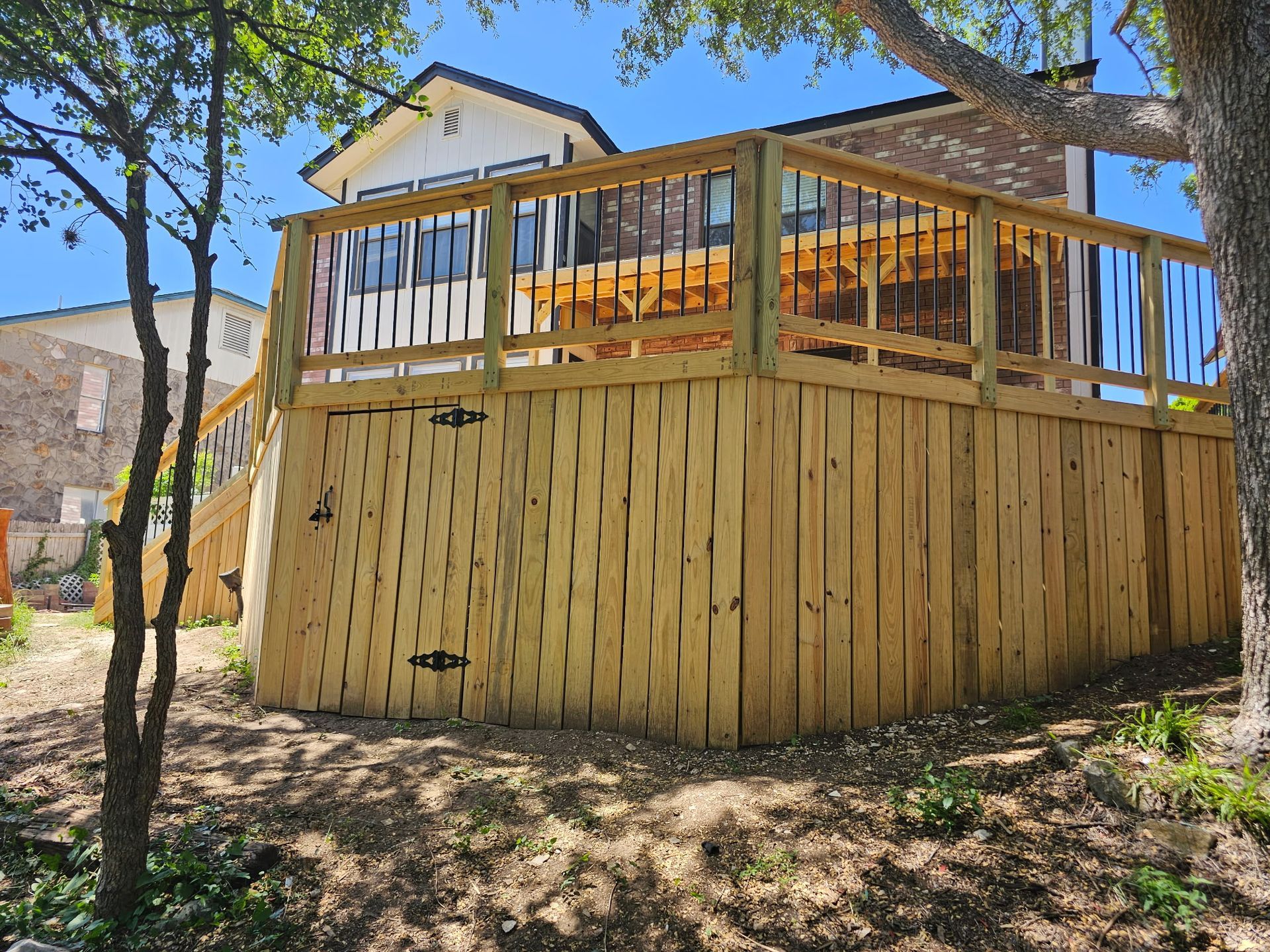 Wooden deck with railing, surrounding a two-story house.