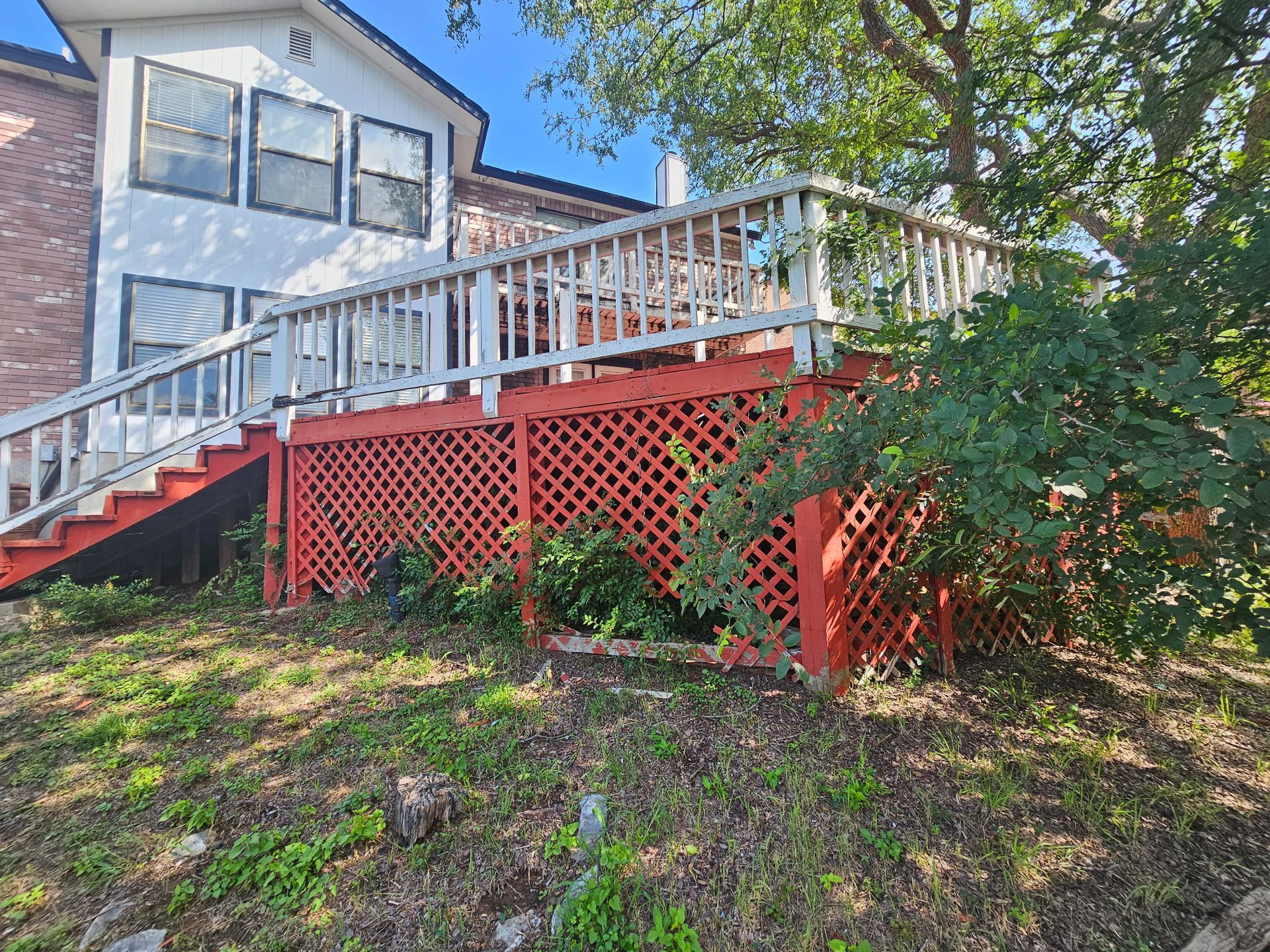 Red and white wooden deck on a hillside, next to a white house with brick accents.