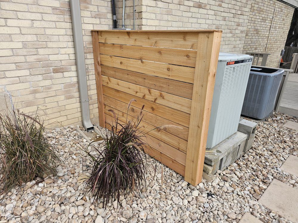A wooden screen partially obscures an outdoor air conditioning unit next to a brick wall.