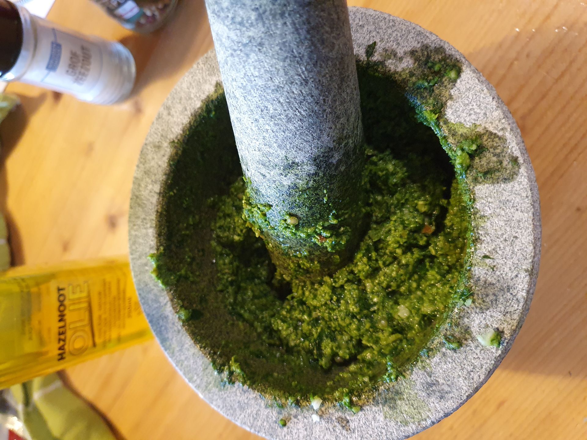 Een vijzel en stamper malen groene pesto op een houten oppervlak.